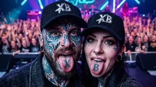 Ein Paar auf einem Konzert streckt die Zunge raus: Beide tragen ein schwarzes Premium Rock Cap aus 100% Bio-Baumwolle mit hochwertigem XB-Stick-Design.