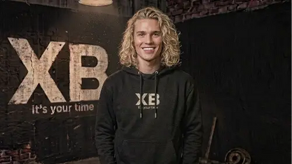Blonder lachender junger Mann trägt schwarzen Premium Rock Hoodie mit hochwertigem XB Design aus Öko-Tex zertifizierten Farben sowie einer Grammatur von 350g/m².