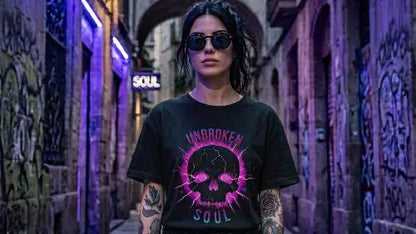 Frau mit schwarzen Haaren und Sonnenbrille in einer Gasse trägt schwarzes Premium Rock T-Shirt aus 100 % Bio-Baumwolle und einer Grammatur von 215g/m² sowie komplexem Unbroken-Skull Design aus Öko-Tex zertifizierten Farben.