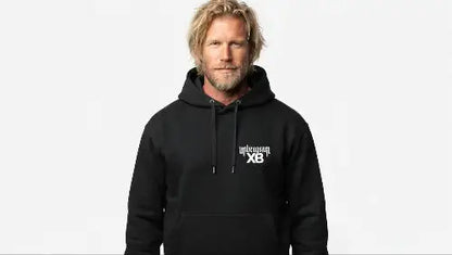 Blonder Mann mit Bart trägt schwarzen Premium Heavyweight Rock Hoodie mit   unbeugsam XB Print.