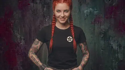 Rothaarige junge Frau mit Zöpfen und Tattoos trägt schwarzes Premium Rock T-Shirt mit XB-Brandig aus Öko-Tex zertifizierten Farben sowie einer Grammatur von 180g/m² aus 100 % Bio-Baumwolle.