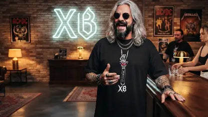 Rockiger Typ an der Bar trägt hochwertiges Premium Rock T-Shirt aus 100% Bio-Baumwolle mit komplexem Skull-Hand-Gitarre Design aus Öko-Tex zertifizierten Farben und einer Grammatur von 240g/m².