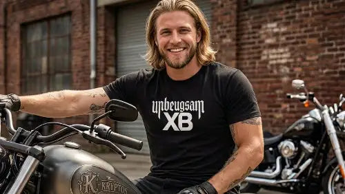 Rocker sitzt lächelnd auf Motorrad und trägt ein schwarzes Premium Rock T-Shirt aus 100 % gekämmter Baumwolle mit markantem Unbeugsam XB Design aus Öko-Tex zertifizierten Farben und einer Grammatur von 185g/m².