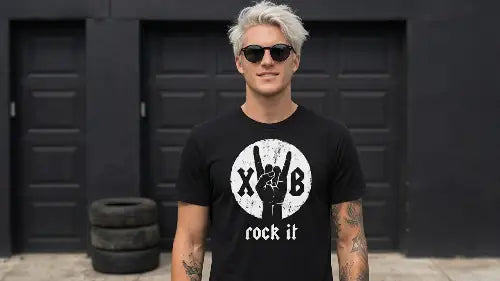 Blonder Mann vor Garage trägt schwarzes Premium Rock T-Shirt aus 100 % gekämmter Baumwolle mit hochwertigem XB-Hand Design aus Öko-Tex zertifizierten Farben sowie einer Grammatur von 185g/m².