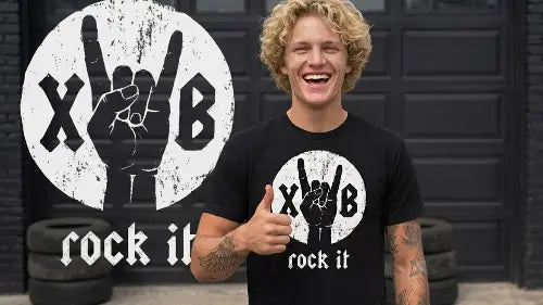 Junger blonder Mann macht den Daumen nach oben und trägt dabei ein hochwertiges schwarzes Premium Rock T-Shirt aus 100% gekämmter Baumwolle mit komplexem rock it Design einer Hand aus Öko-Tex zertifizierten Farben sowie einer Grammatur von 185g/m².