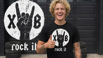 Junger blonder Mann macht den Daumen nach oben und trägt dabei ein hochwertiges schwarzes Premium Rock T-Shirt aus 100% gekämmter Baumwolle mit komplexem rock it Design einer Hand aus Öko-Tex zertifizierten Farben sowie einer Grammatur von 185g/m².