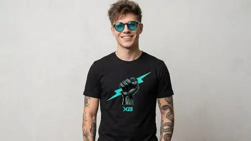 Tätowierter Mann im schwarzen Premium Rock T-Shirt mit Unyielding-Spirit-Bitz-Faust-Print und türkiser Sonnenbrille vor neutralem Hintergrund.