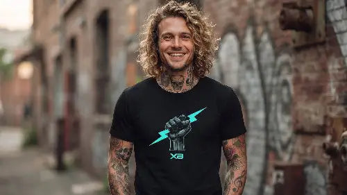 Blonder, tätowierter Mann mit lockigem Haar und strahlendem Lachen trägt ein schwarzes Premium Rock T-Shirt mit türkisfarbenem Blitz-Faust-Design.