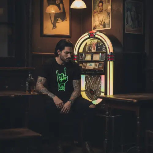 Mann sitzt allein an Musikbox und trägt ein Premium Rock T-Shirt für Männer mit Devilshorn-Hand-Design.