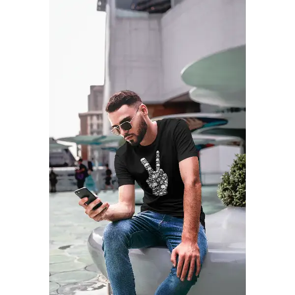 Wartender Mann mit Smartphone trägt ein Rock T-Shirt für Männer mit komplexem Hand-Skull-Design-Peace.