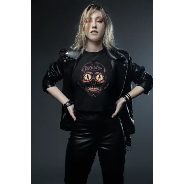 Eine junge Dame trägt ein Rock T-Shirt für Frauen.Das schwarze Damen Premium T-Shirt hat den Aufdruck eines Totenkopfes in dessen leuchtenden Augen Frauen tanzen sowie die Aufschrift Rockstar.