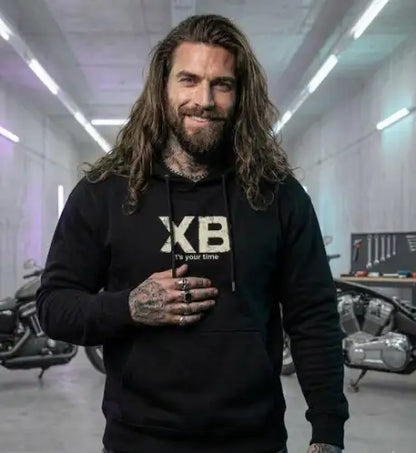 Mann in Garage trägt einen 350g/m² Heavyweight-Premium-Rock-Hoodie von XB in Schwarz.